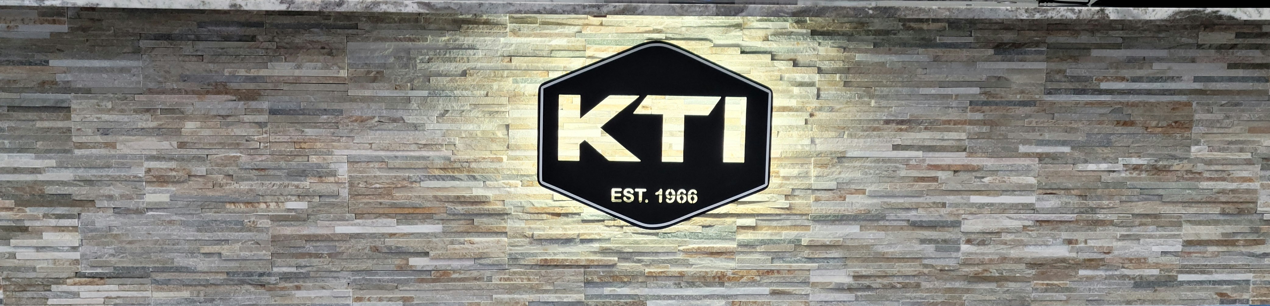 The KTI hexagon emblem mounted on a stacked-stone wall &mdash; the registered Kenjura Tile, Inc. mark.