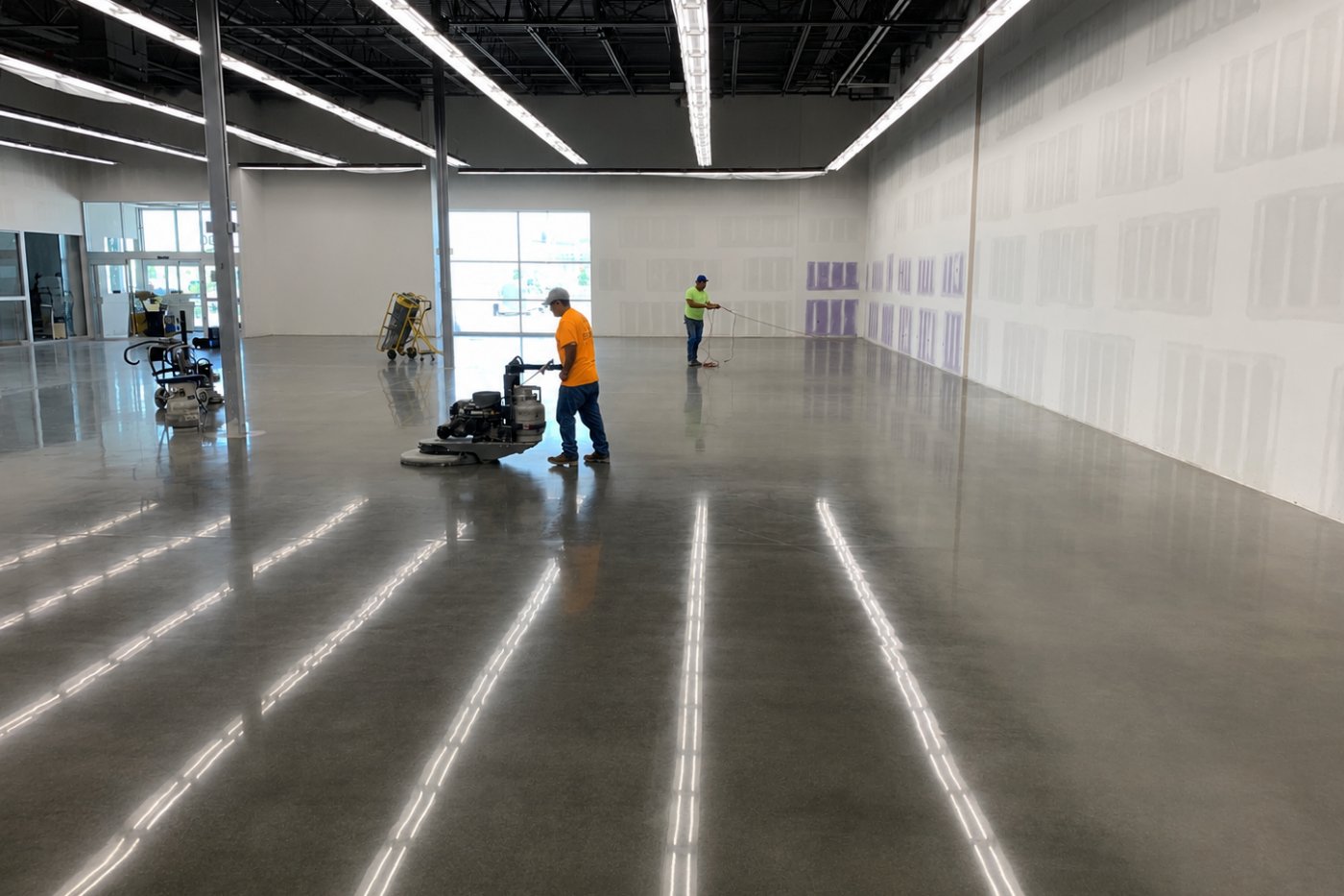 Kenjura Tile crew running diamond-polishing machines across a large commercial concrete floor during an active buildout.