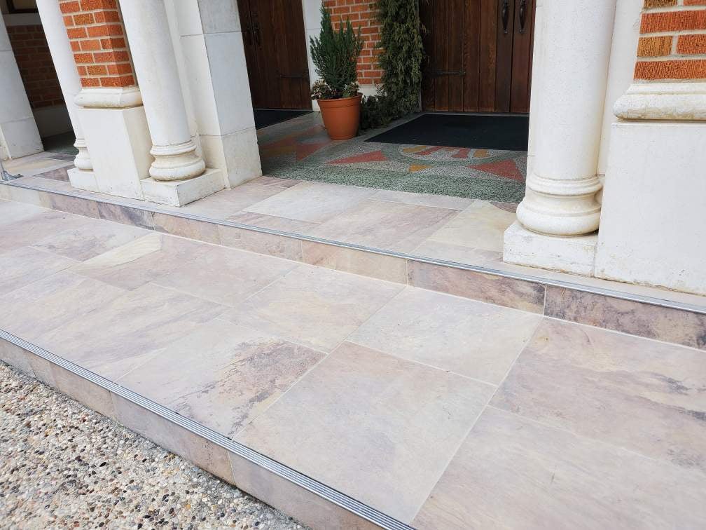 Stone-tile entry steps installed by Kenjura Tile at a historic church &mdash; precision-cut treads, joint lines, and exposed-aggregate transitions, all properly finished and ramped.