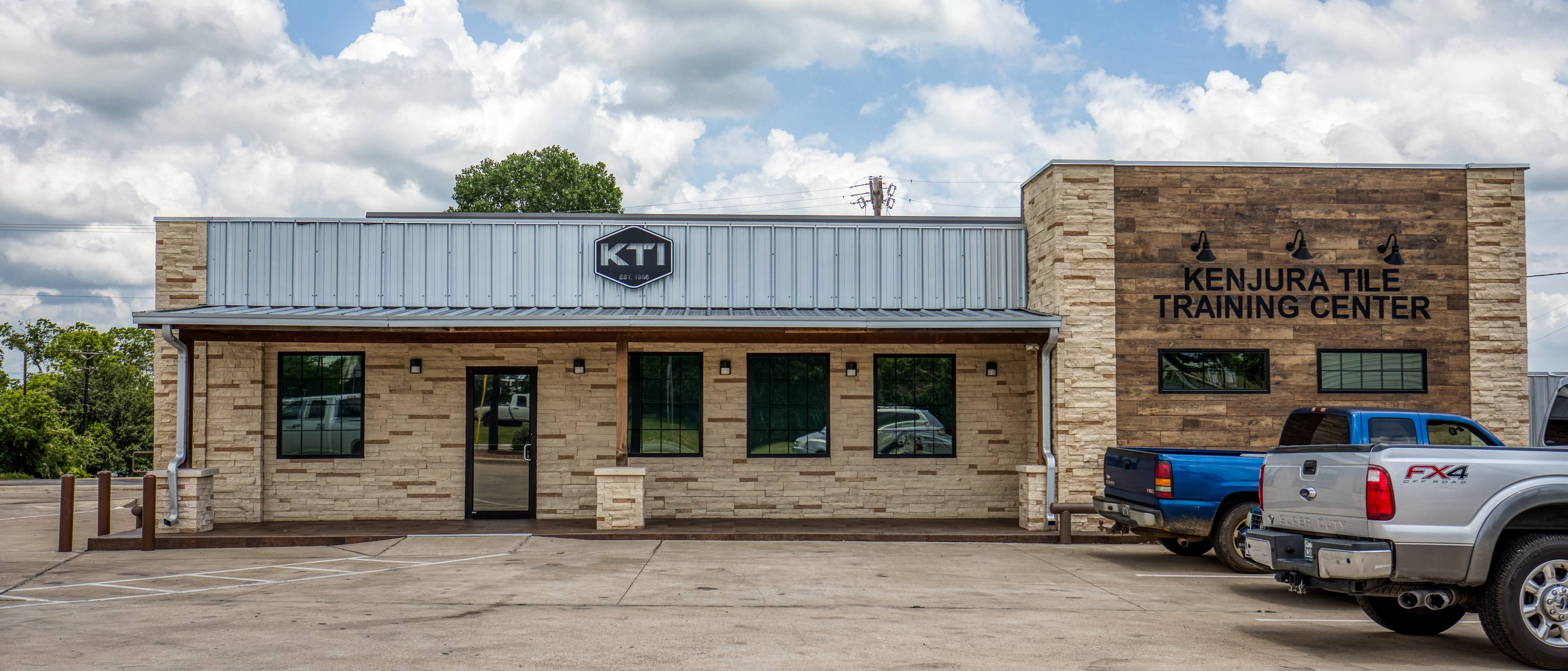 Full exterior view of the Kenjura Tile Training Center building in Brenham, Texas, with reclaimed-wood facade and signage.