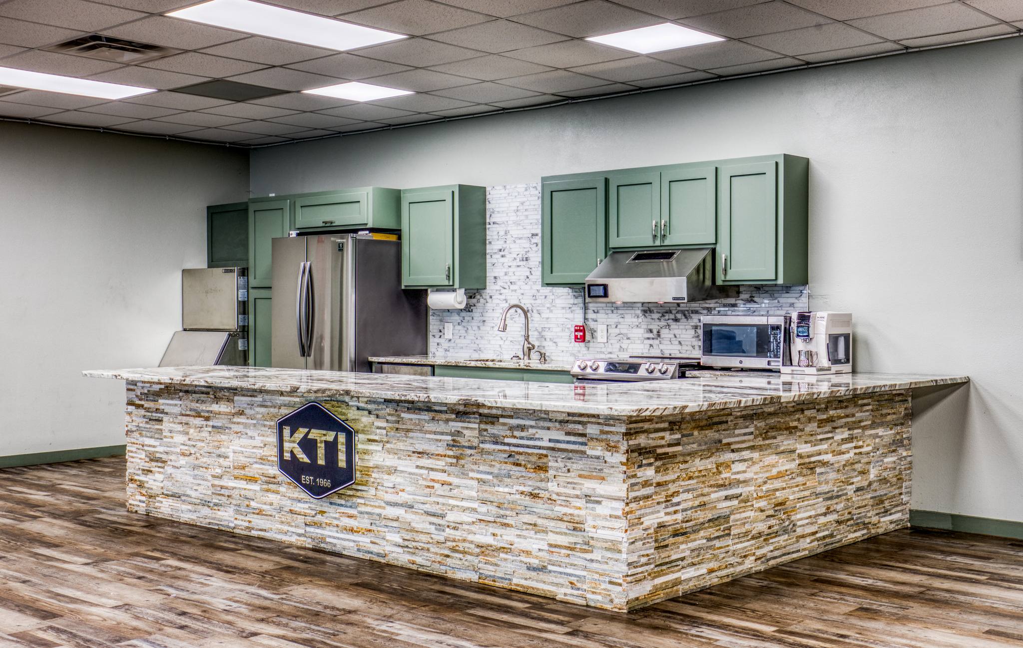 Full kitchen with stone-clad bar featuring the KTI hexagon emblem, marble counter, and adjacent stainless appliances.