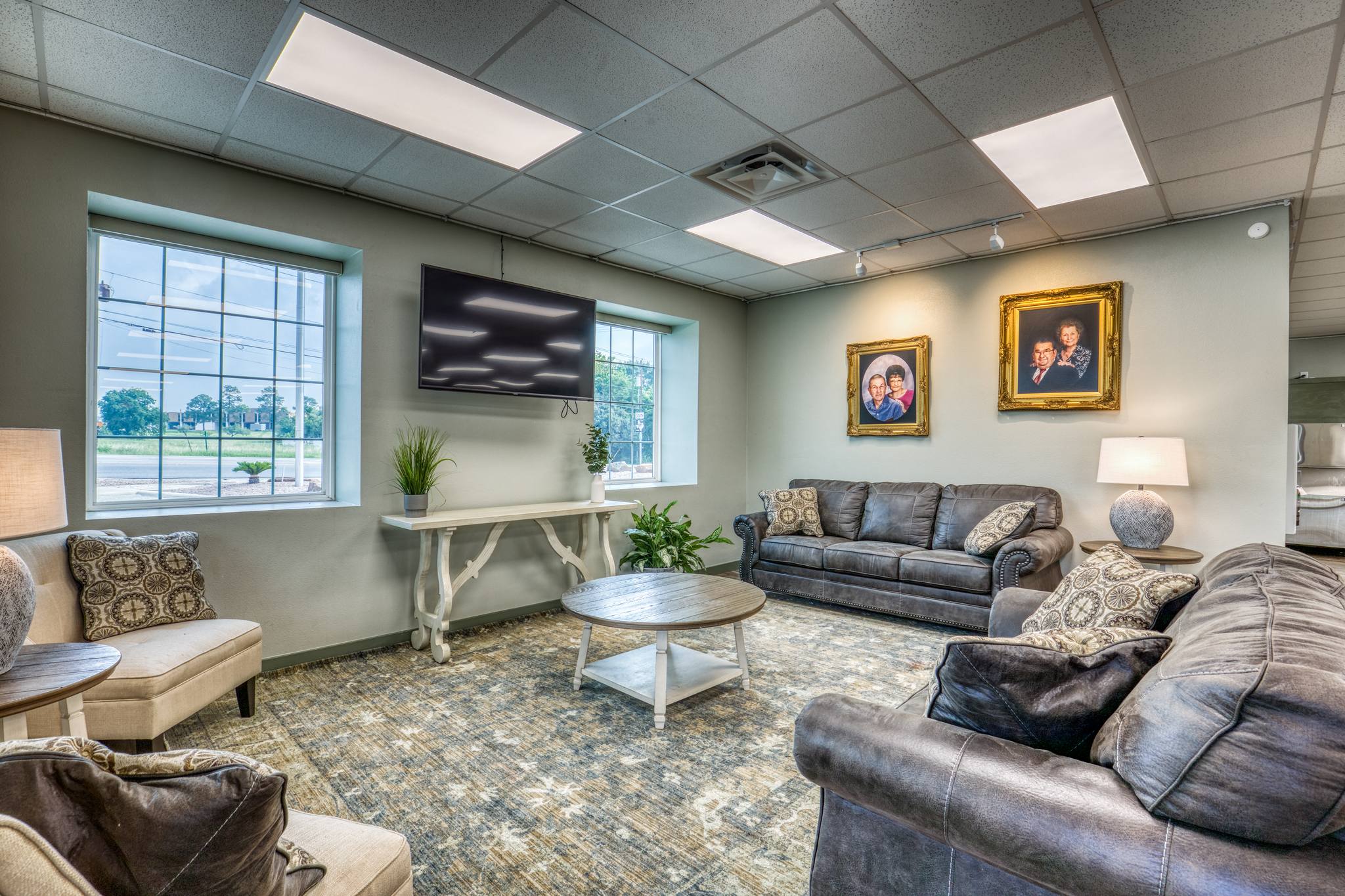 Lounge area with comfortable seating, area rug, wall-mounted television, and framed family portraits commemorating the Kenjura family heritage.