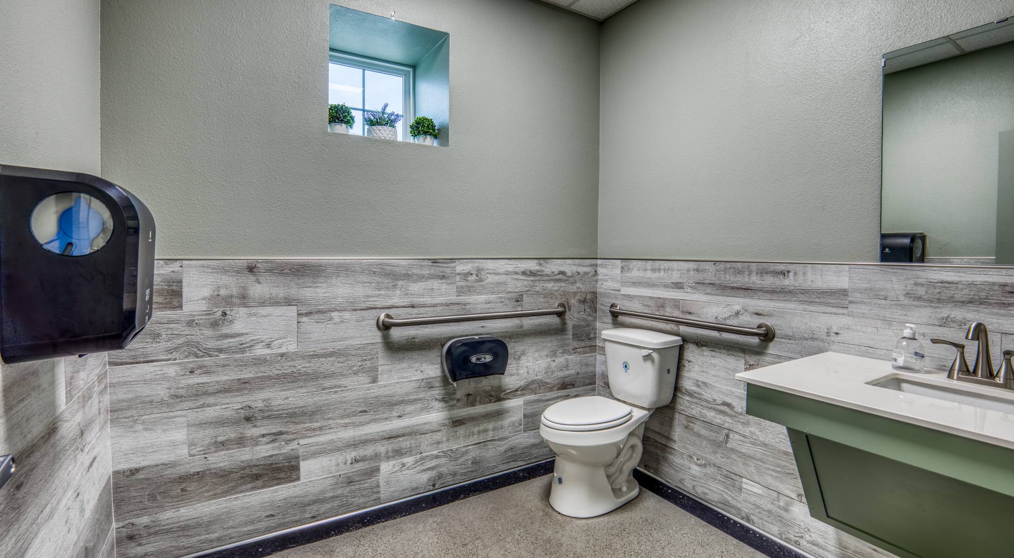 ADA-accessible restroom with wood-look plank wall tile, accessible grab bars, and modern fixtures.