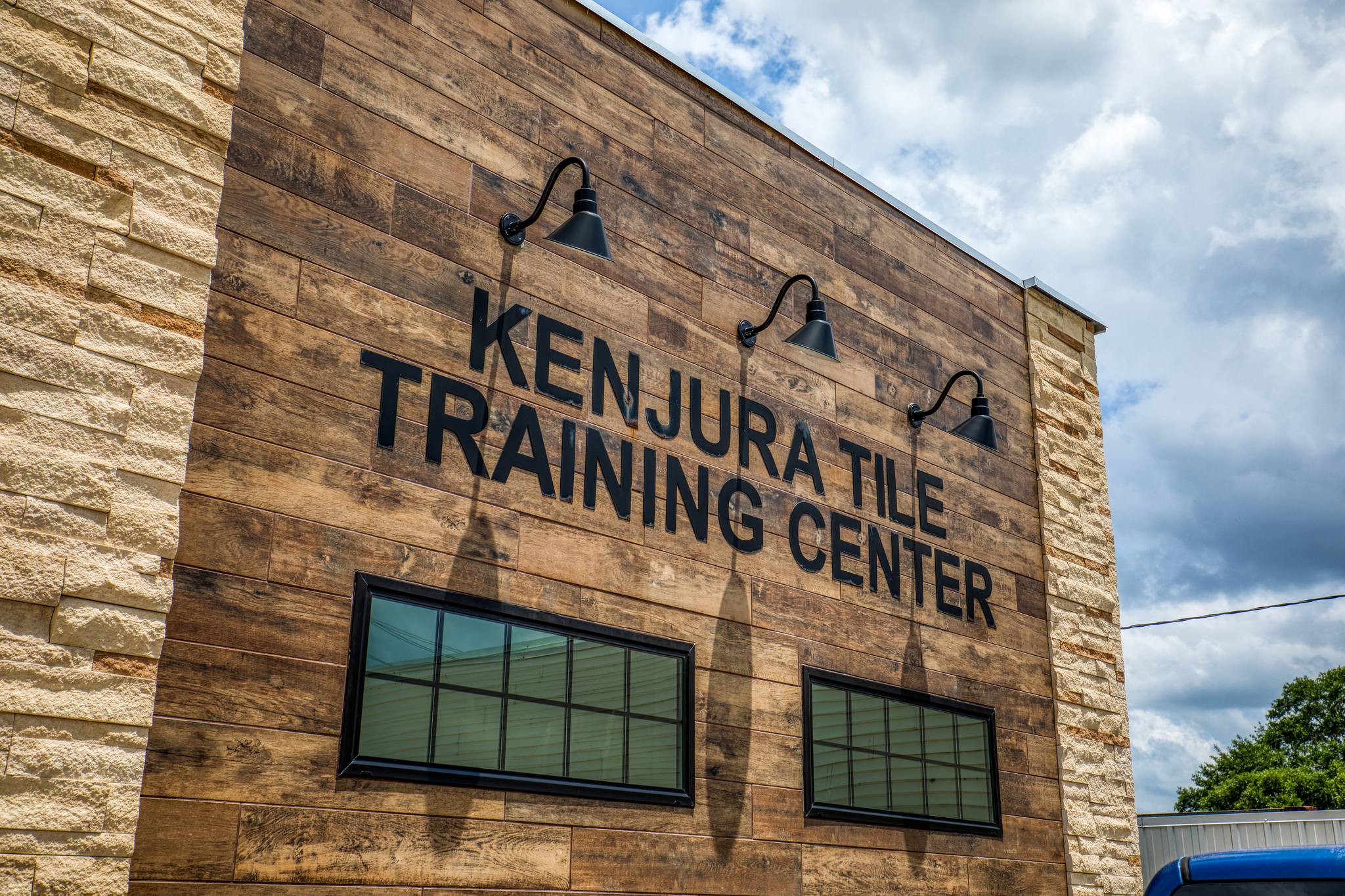 Kenjura Tile Training Center exterior signage on reclaimed-wood facade with industrial gooseneck lighting.